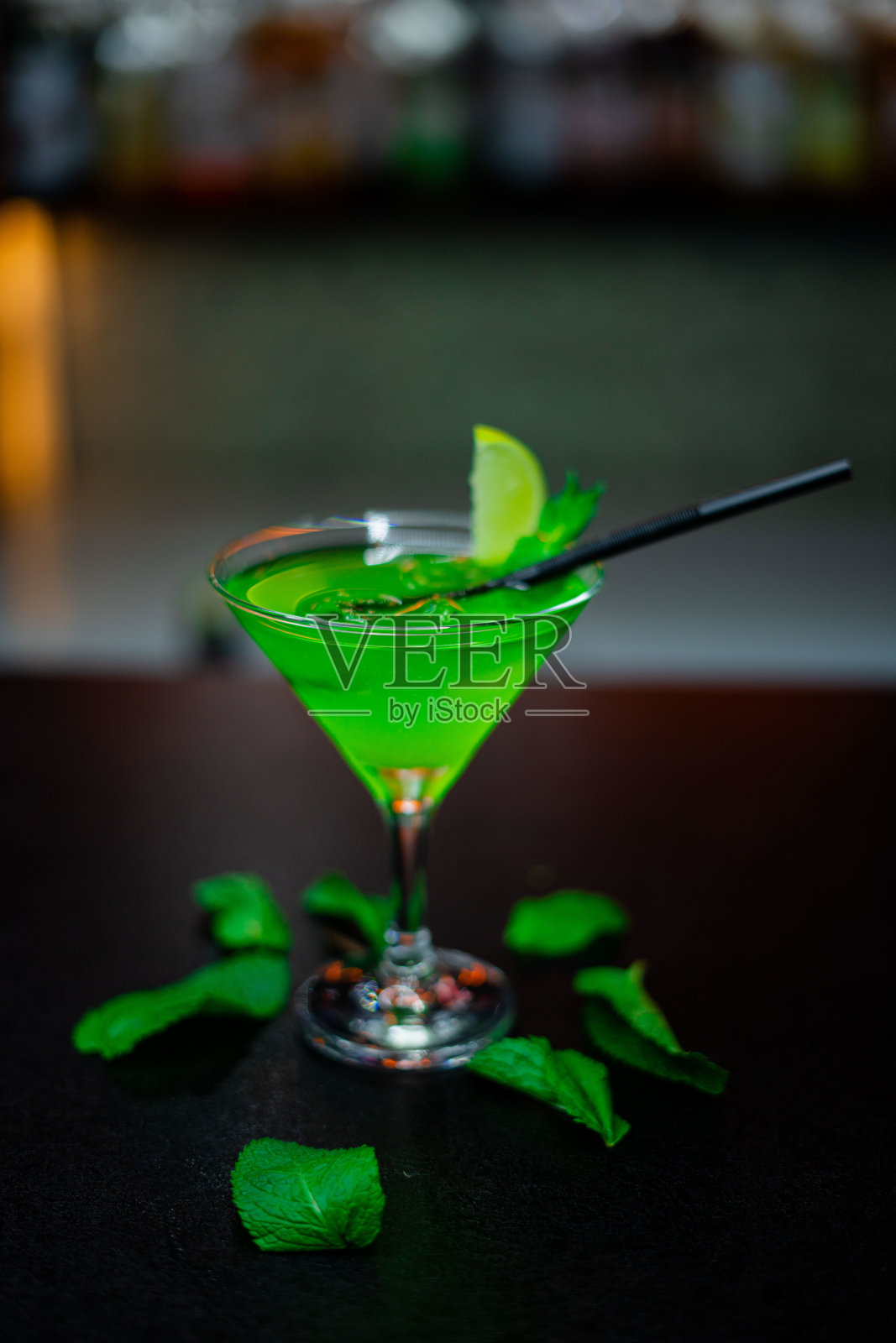 一杯加薄荷和柠檬的绿色鸡尾酒放在吧台上。有选择性的重点照片摄影图片