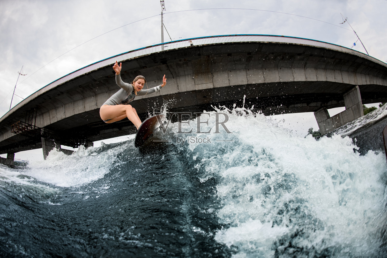 年轻的金发女郎骑在冲浪板上。桥在背景照片摄影图片