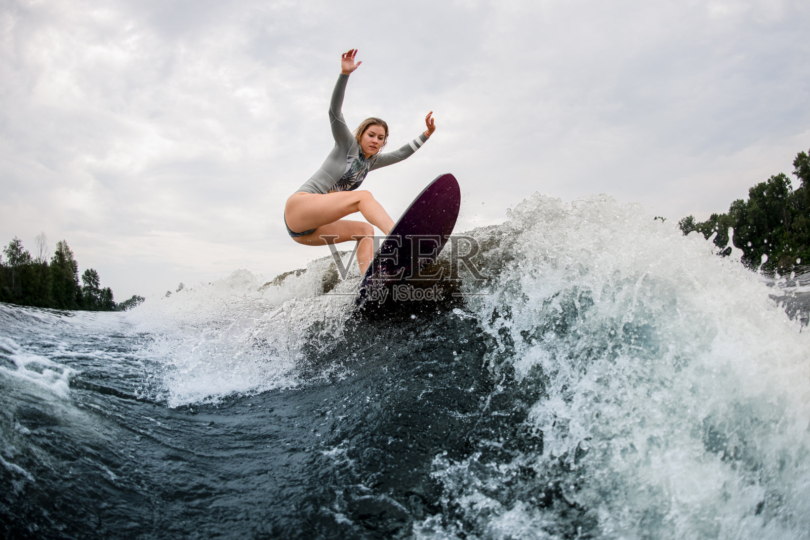 活跃的湿女人在灰色的潜水衣水上冲浪在巨大的溅起的波浪照片摄影图片