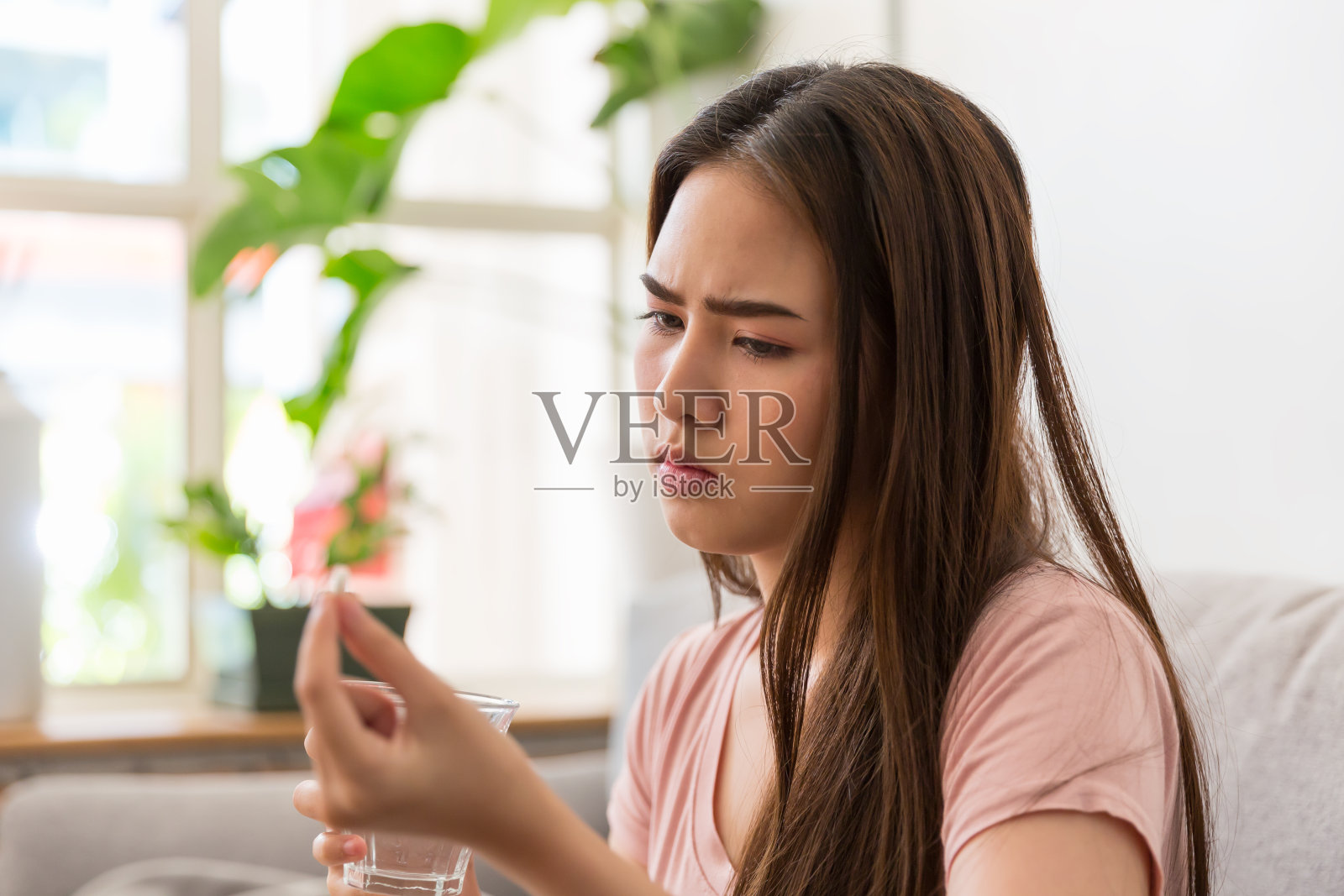 年轻的亚洲妇女感觉不舒服，坐在家里的沙发上吃药。亚洲女人紧张和生病照片摄影图片