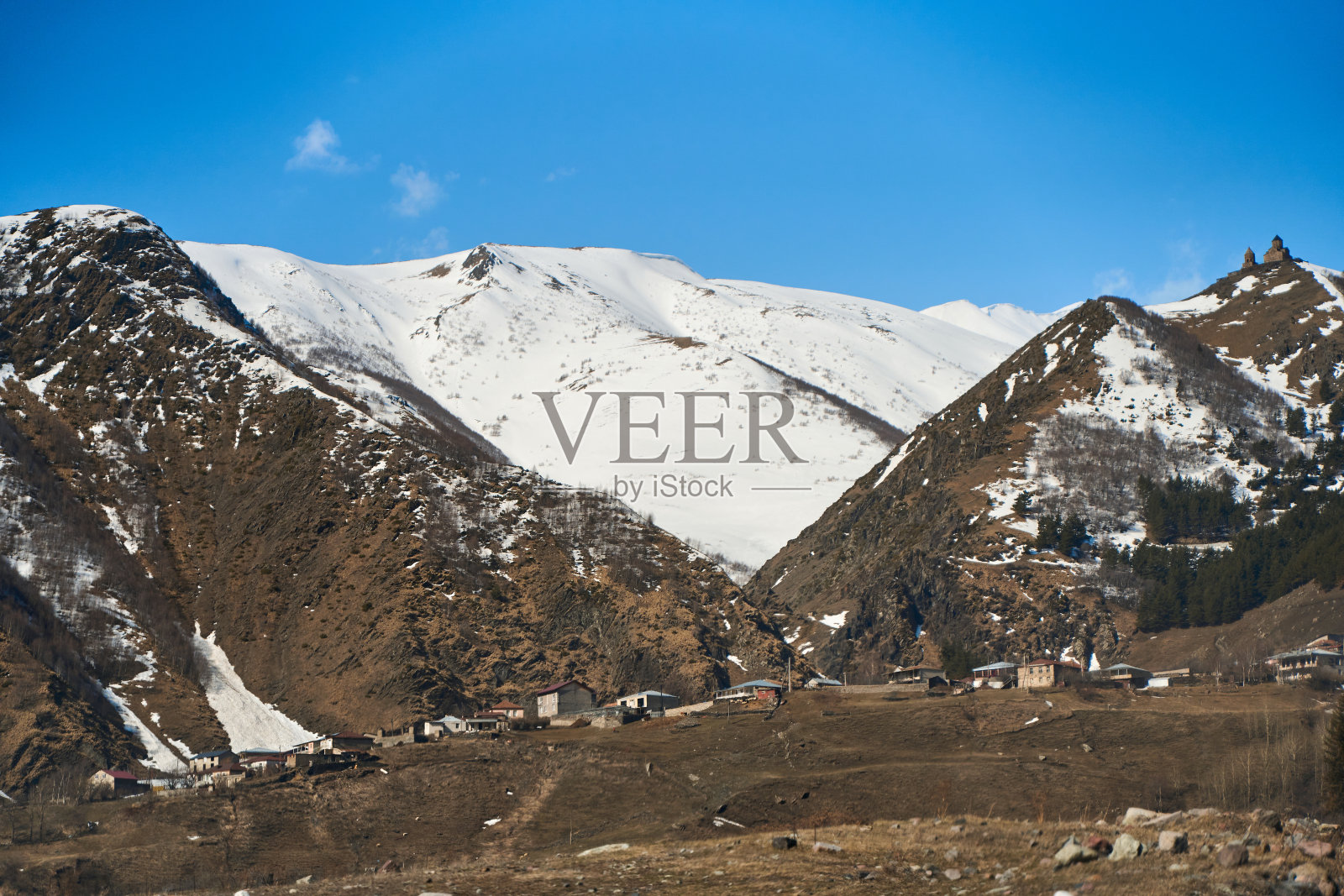 早春。这个村庄在山里。山顶上的雪冠。脚下的小村庄照片摄影图片