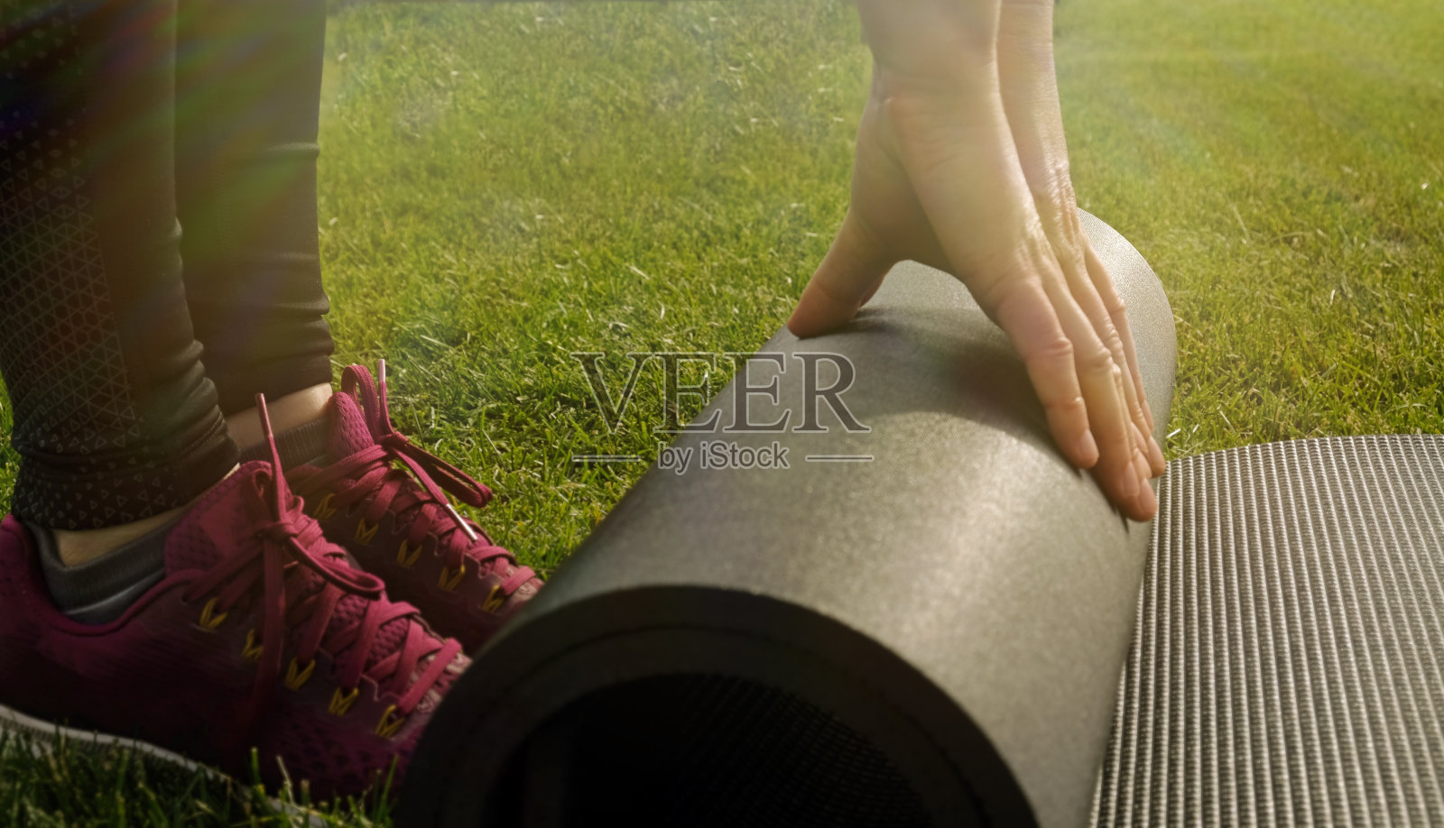 年轻的运动女子折叠灰色的健身垫后健身在绿色的草坪。在后院或公园的绿色草坪上准备瑜伽体式的妇女。跑步前热身。健康的生活方式。照片摄影图片