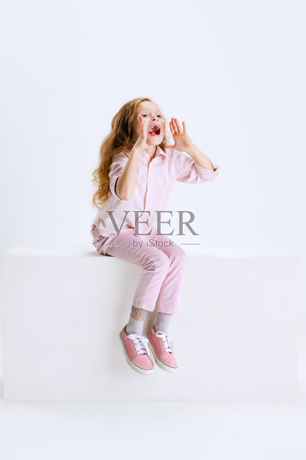 摄影棚拍摄的可爱美丽的女孩，长发飘逸，穿着休闲装，坐在白色背景的大盒子上。照片摄影图片