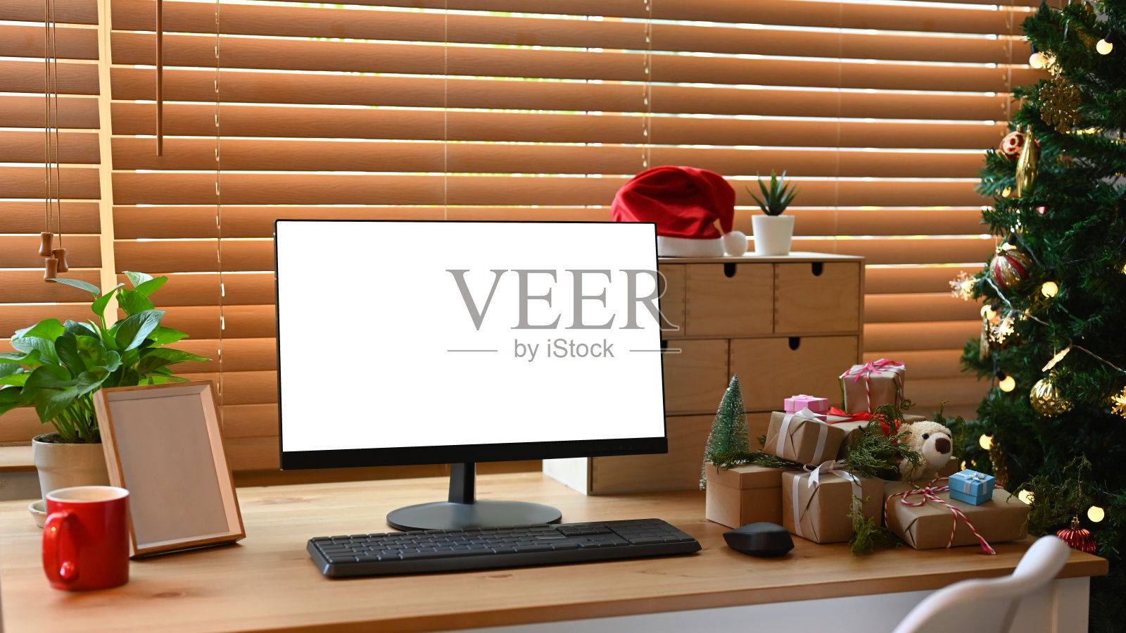 客厅里圣诞树旁的木桌上放着电脑、礼品盒和咖啡杯。照片摄影图片