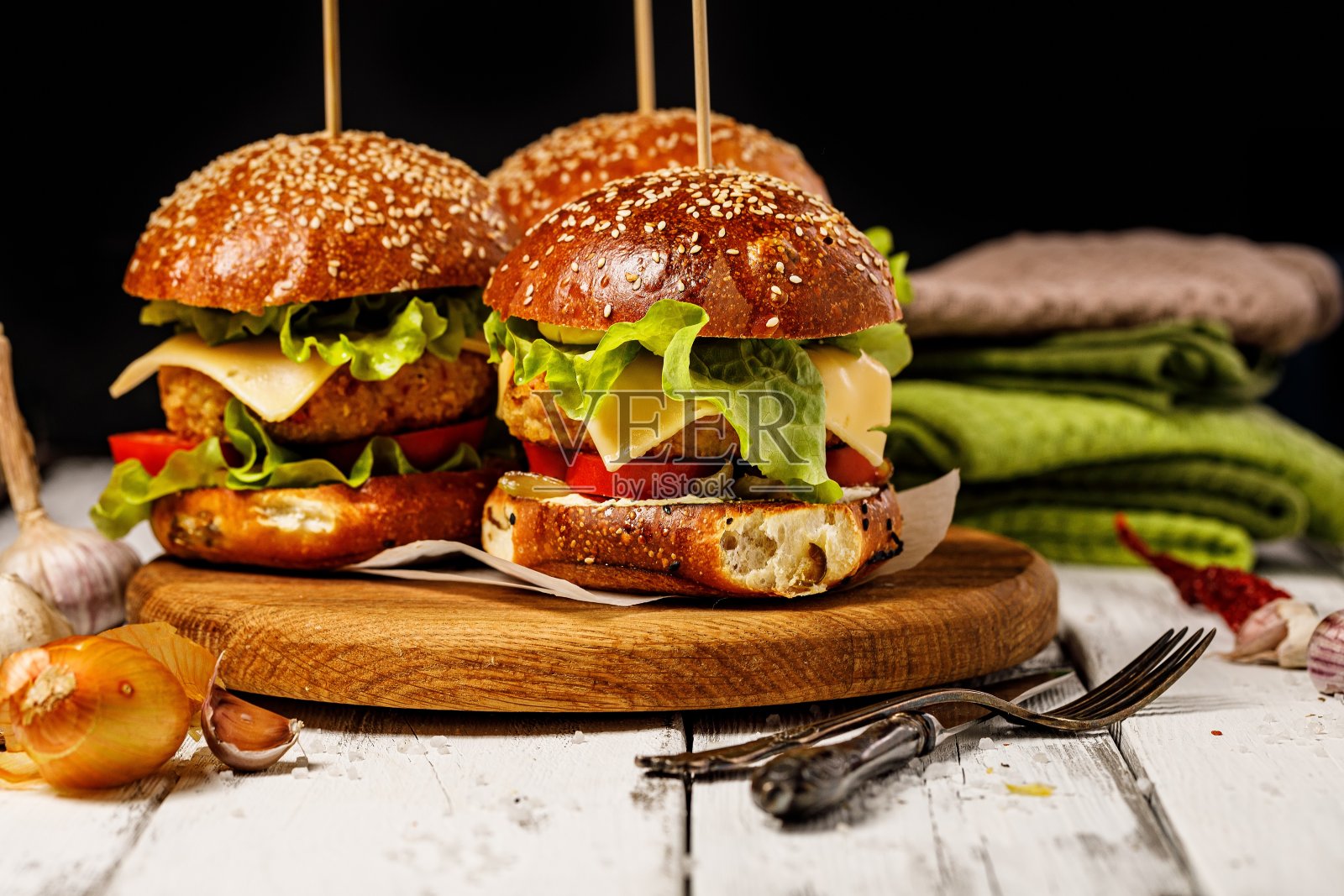 自制美味鸡肉汉堡配奶酪，新鲜沙拉和蔬菜放在圆形切菜板上。生菜叶子，西红柿和洋葱。传统的美国快餐。乡村背景。本空间照片摄影图片