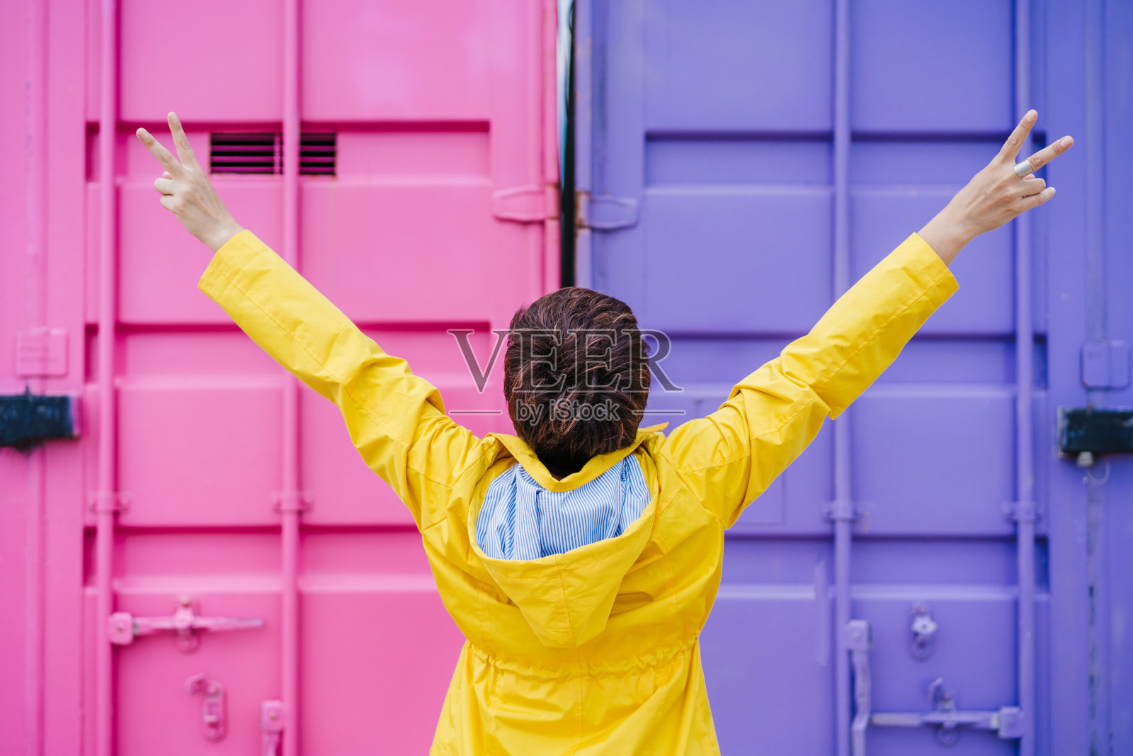 女人的背影，在粉红色和紫色的背景下，穿着黄色雨衣，双臂高举。丰富多彩的户外生活方式照片摄影图片