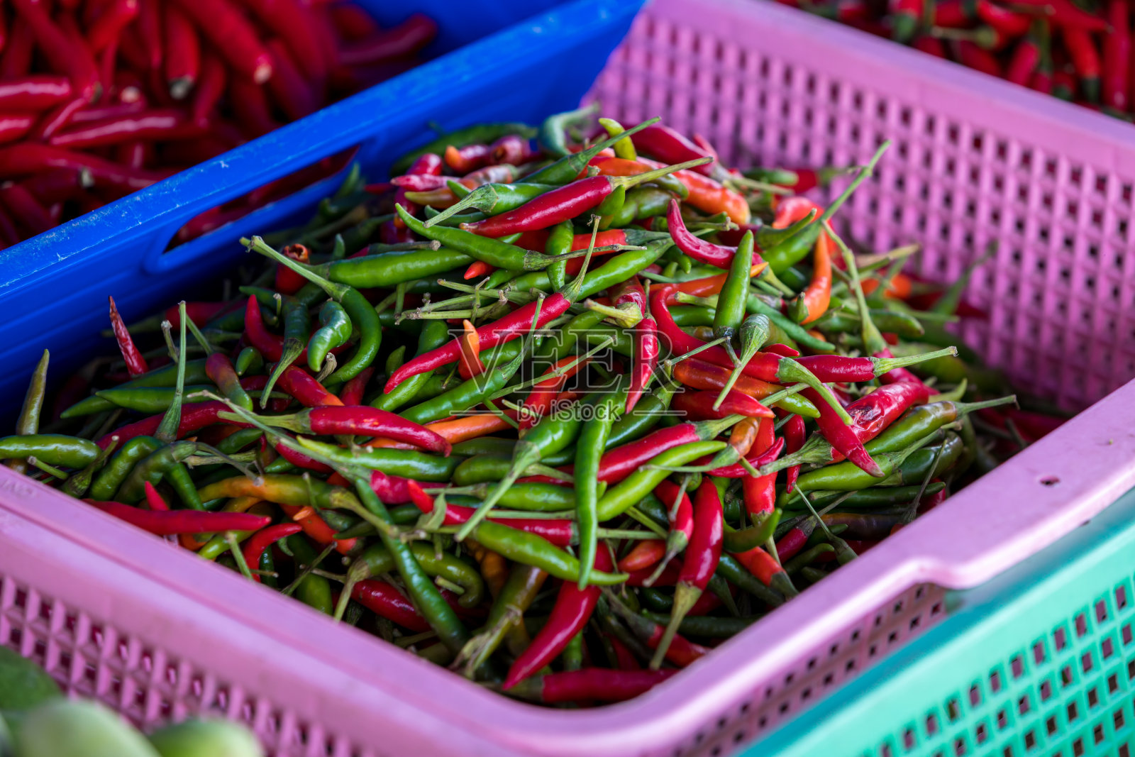 绿色和红色的辣椒在塑料篮子在新鲜市场出售。五颜六色的辣椒摊在新鲜的市场上。泰国街头小吃中的泰国辣椒。照片摄影图片