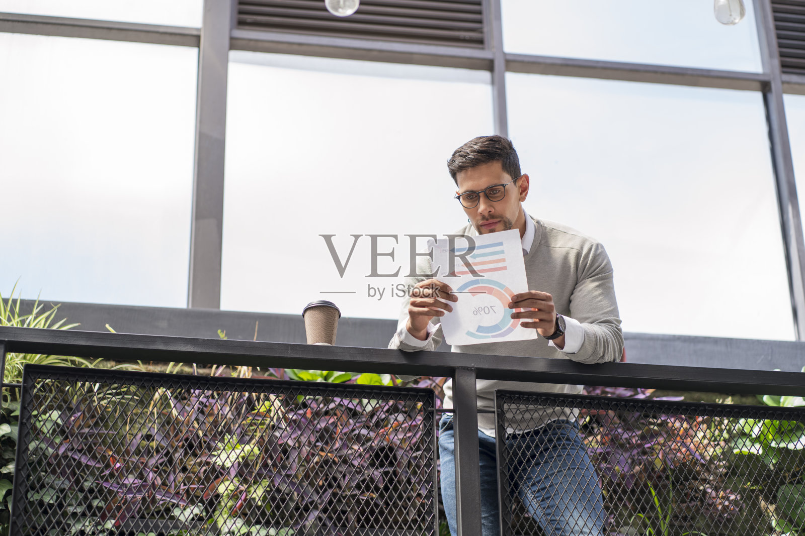 一个拉丁裔男子发现自己在他工作的办公室里，靠在办公室二楼的栏杆上阅读公司文件照片摄影图片