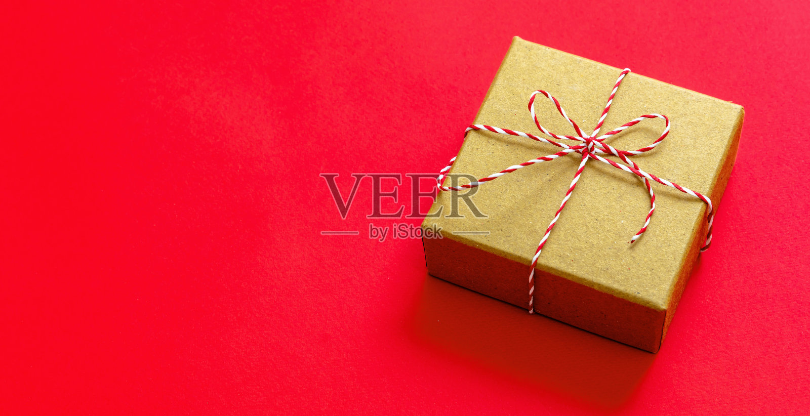 圣诞礼品盒上的红色背景。红白条纹串系在棕色牛皮纸礼物。照片摄影图片