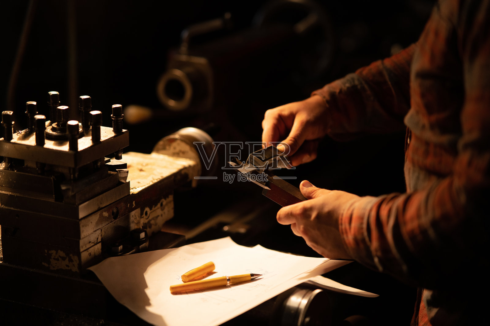 工业工人用卡尺测量钢构件的尺寸，在夜间金属车间室内。照片摄影图片