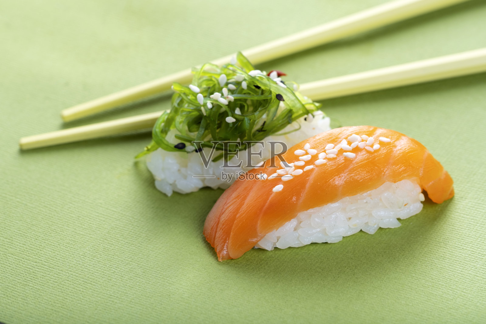 两种不同的寿司，绿色的背景上有三文鱼和海藻，手握清酒和竹节照片摄影图片