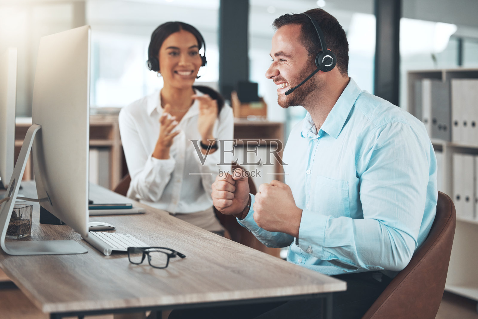 一名年轻的呼叫中心工作人员与同事坐在办公室庆祝成功照片摄影图片