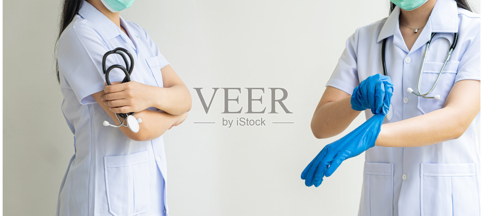 图为，一名女医生站在诊所的办公室里，身穿白色衣服，双手交叉在白色背景上。年轻女医生戴着手套照片摄影图片