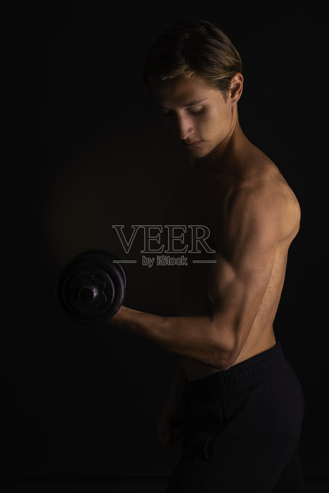 年轻运动员在练习二头肌时，用左臂握哑铃的身体轮廓，研究他的结果。照片摄影图片