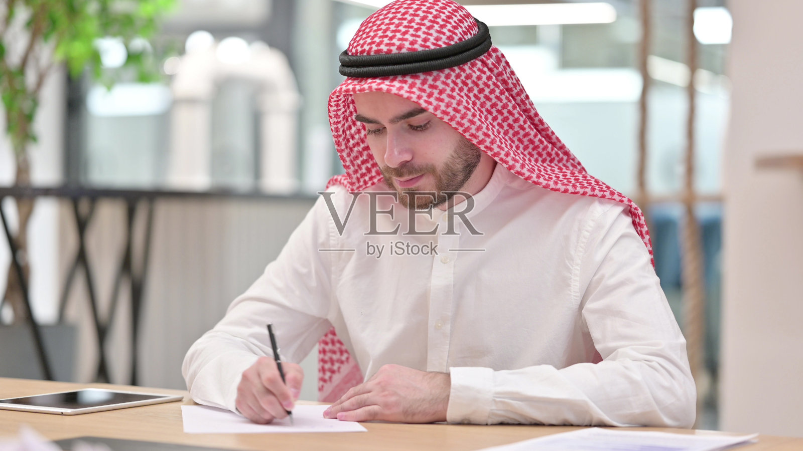 专注的阿拉伯商人在办公室的纸上写作照片摄影图片