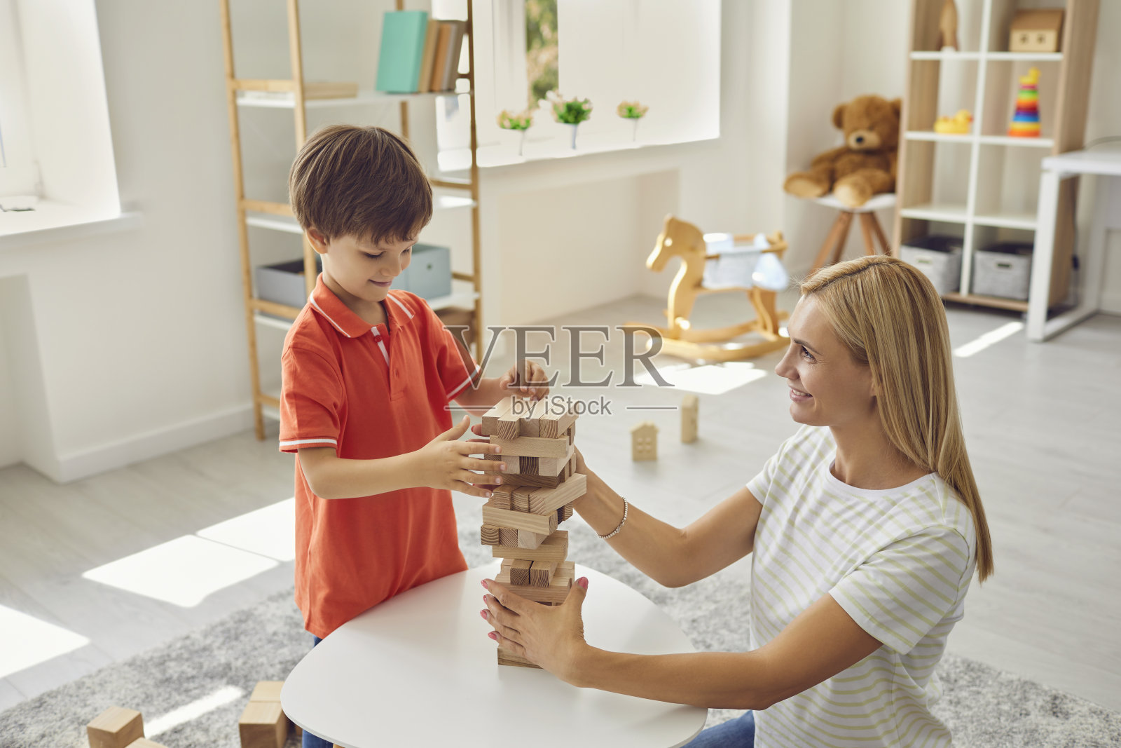 快乐的妈妈帮微笑的儿子在家里建造木金字塔的部件照片摄影图片
