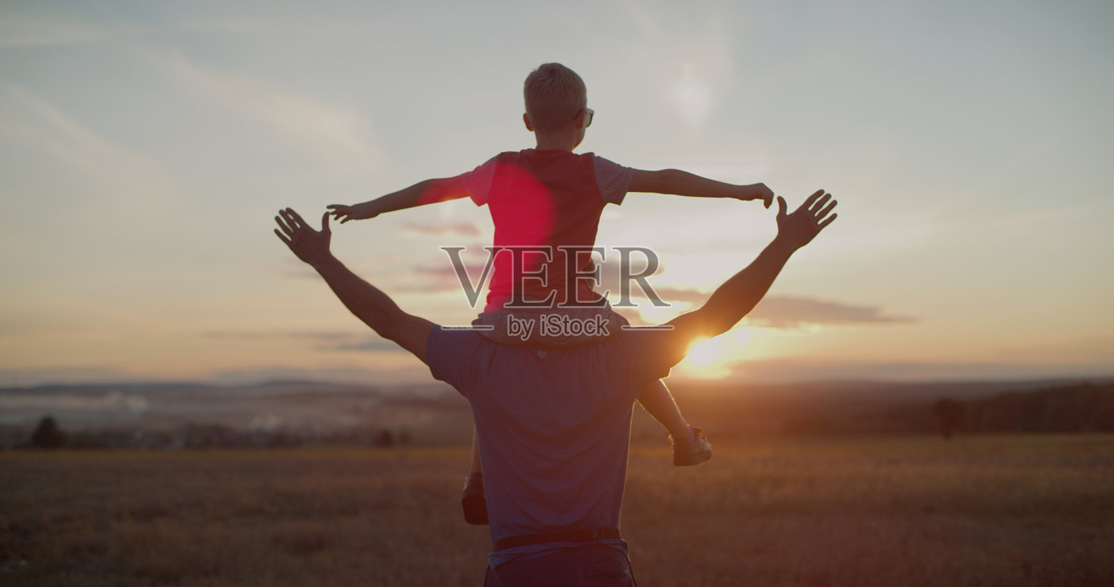 爸爸把儿子抱在肩上。他们张开双臂，在日落的天空下享受自由照片摄影图片