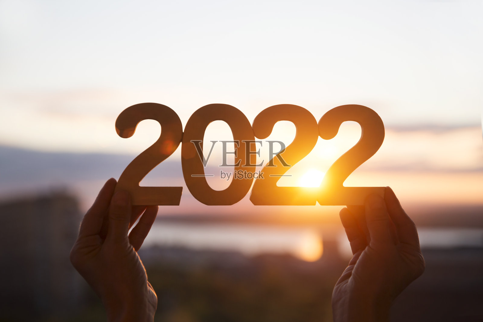 手拿着木制数字“2022”，背景是日落的天空。生态。新年快乐概念。副本的空间。圣诞快乐照片摄影图片