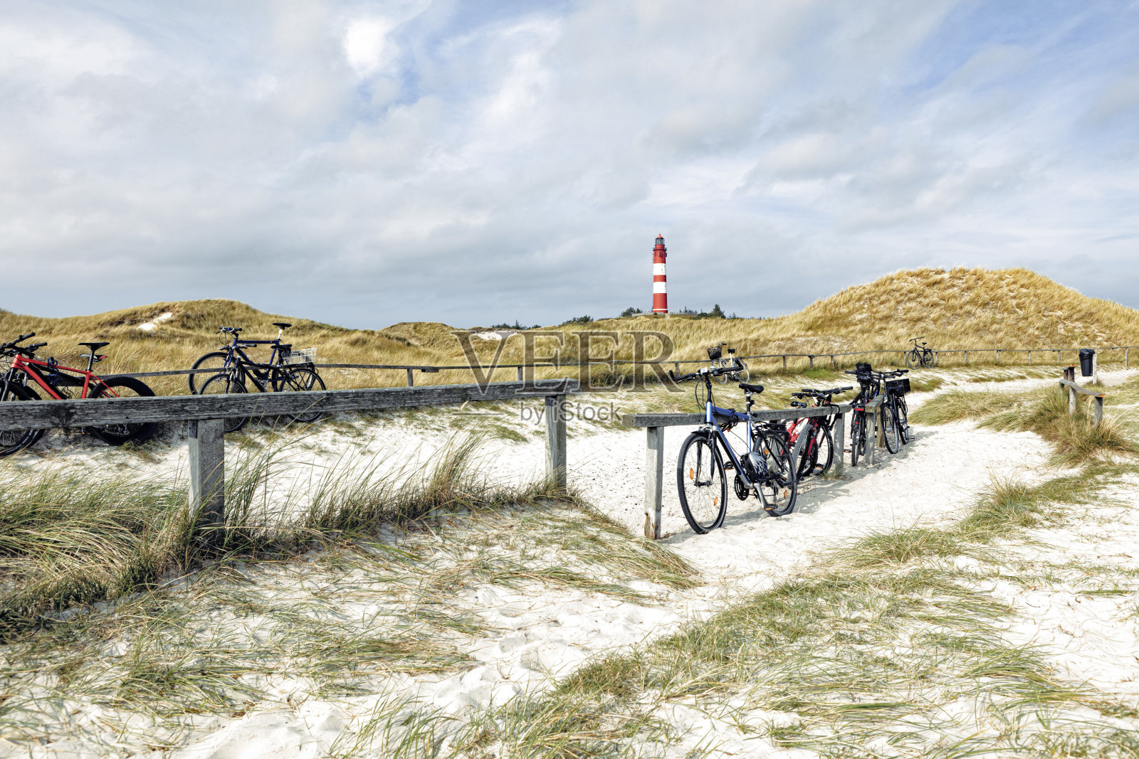 几辆不同的自行车靠在指定的自行车停放处的木架子上。背景是高大的红白条纹灯塔。照片摄影图片