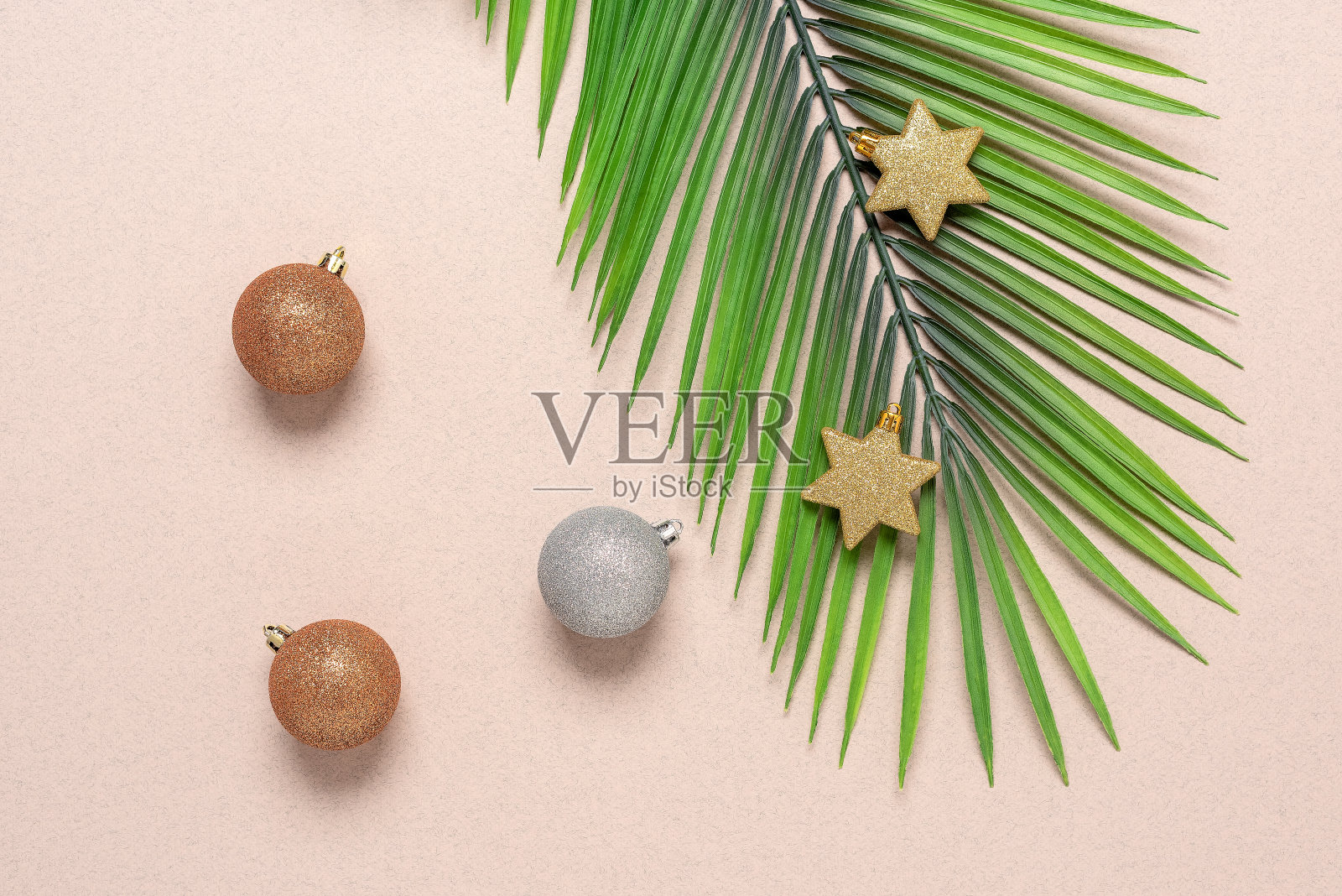 人造棕榈叶、圣诞球和米色牛皮纸上的星星。圣诞组成。俯视图，平躺照片摄影图片