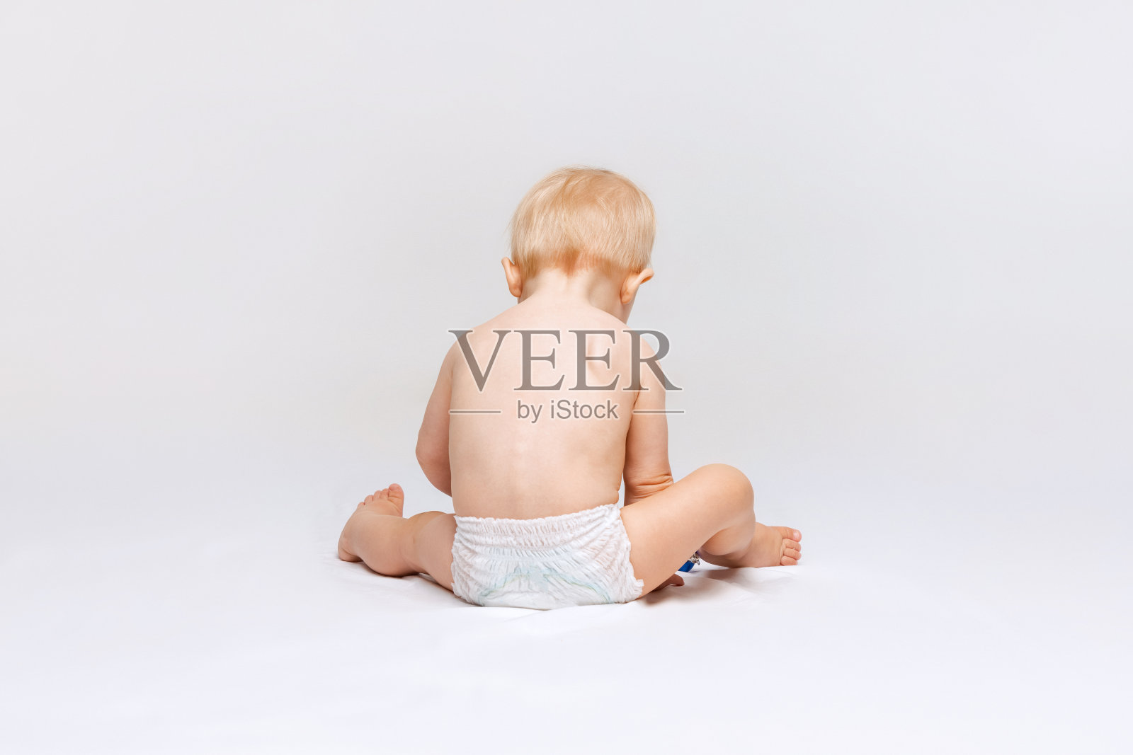 全身后视镜的小可爱的蹒跚学步的女孩，婴儿平静地坐在尿布和玩孤立的白色工作室背景。照片摄影图片