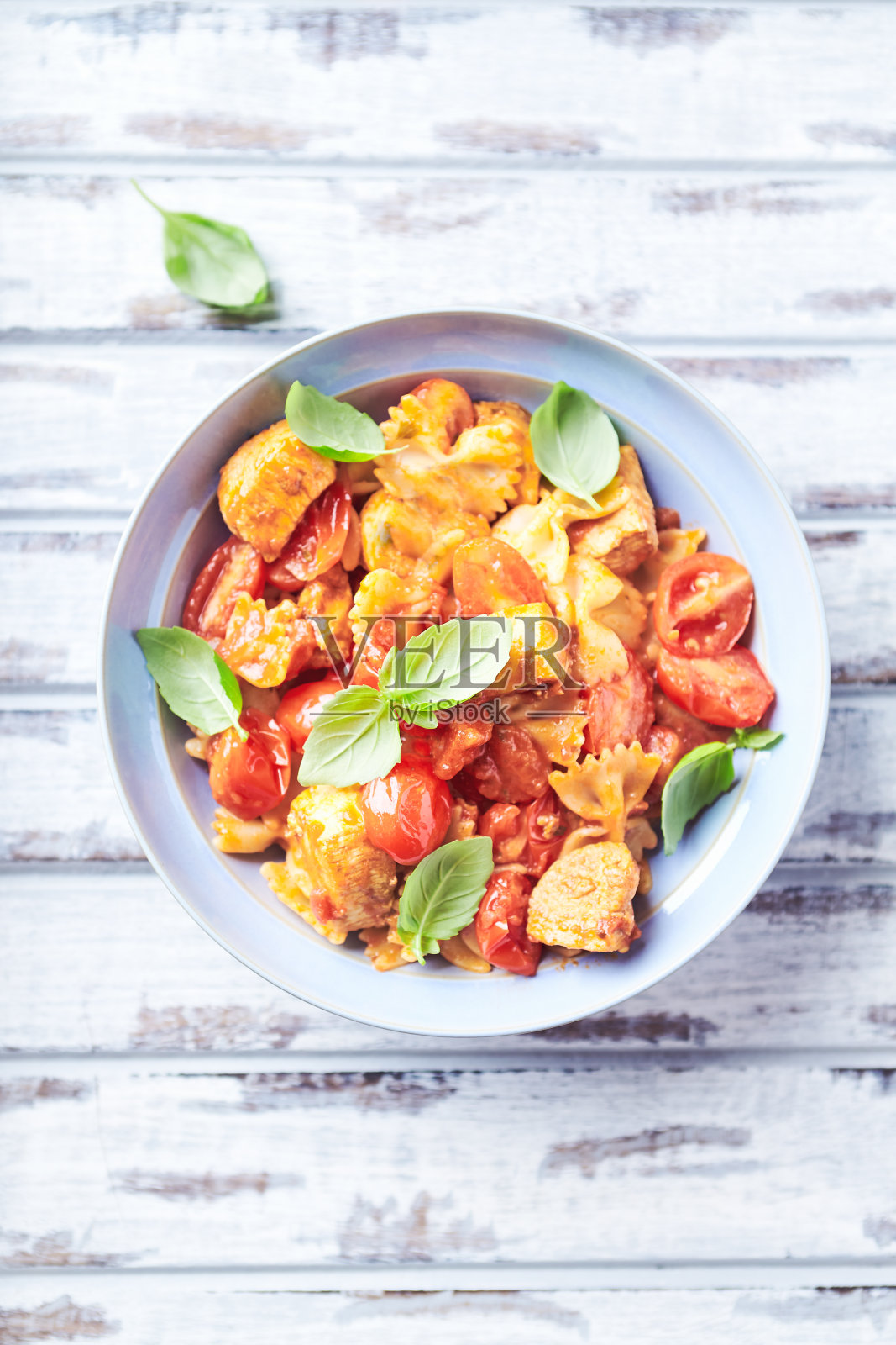法尔法意大利面配鸡胸肉，樱桃番茄和新鲜罗勒。明亮的木制背景。前视图。照片摄影图片