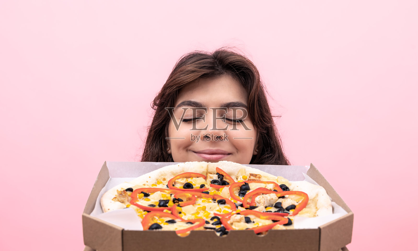 迷人的女孩享受新鲜出炉的披萨在粉红色的背景上的味道。照片摄影图片