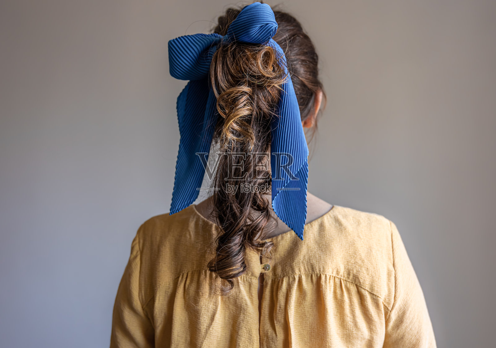 后视图，一个女孩穿着裙子，头发上戴着蝴蝶结，背景是灰色的。照片摄影图片