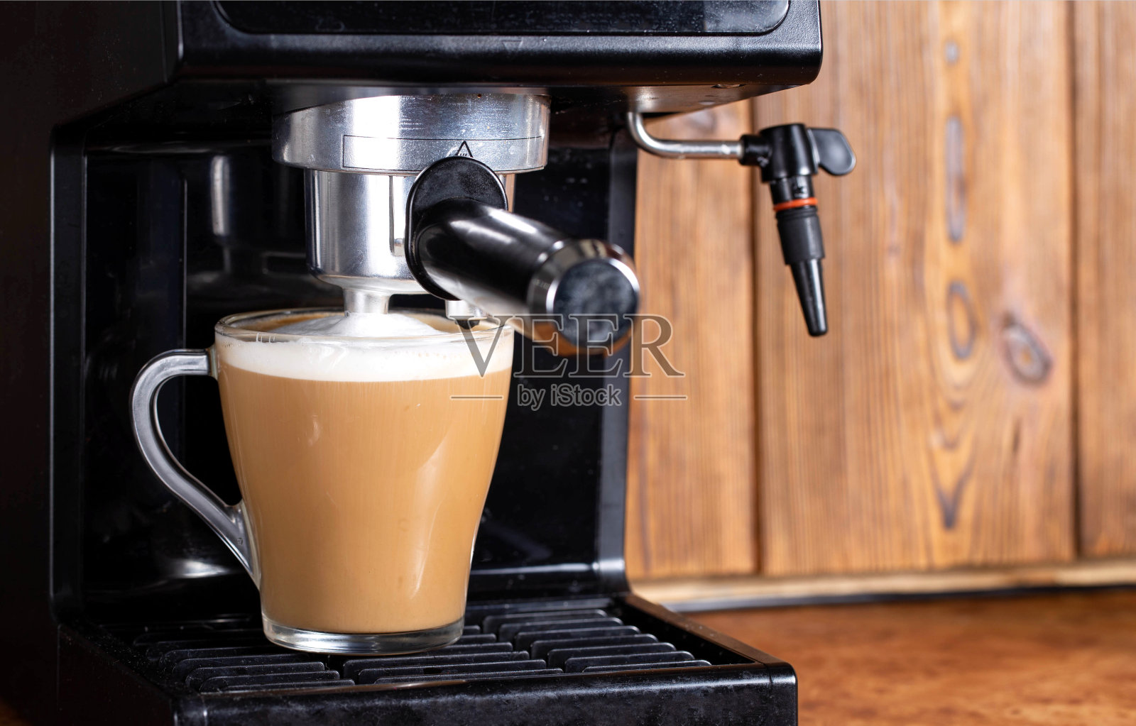 在卡布奇诺咖啡机里用卡布奇诺牛奶煮咖啡，木制桌面背景上有一个手动卡布奇诺机。特写镜头照片摄影图片