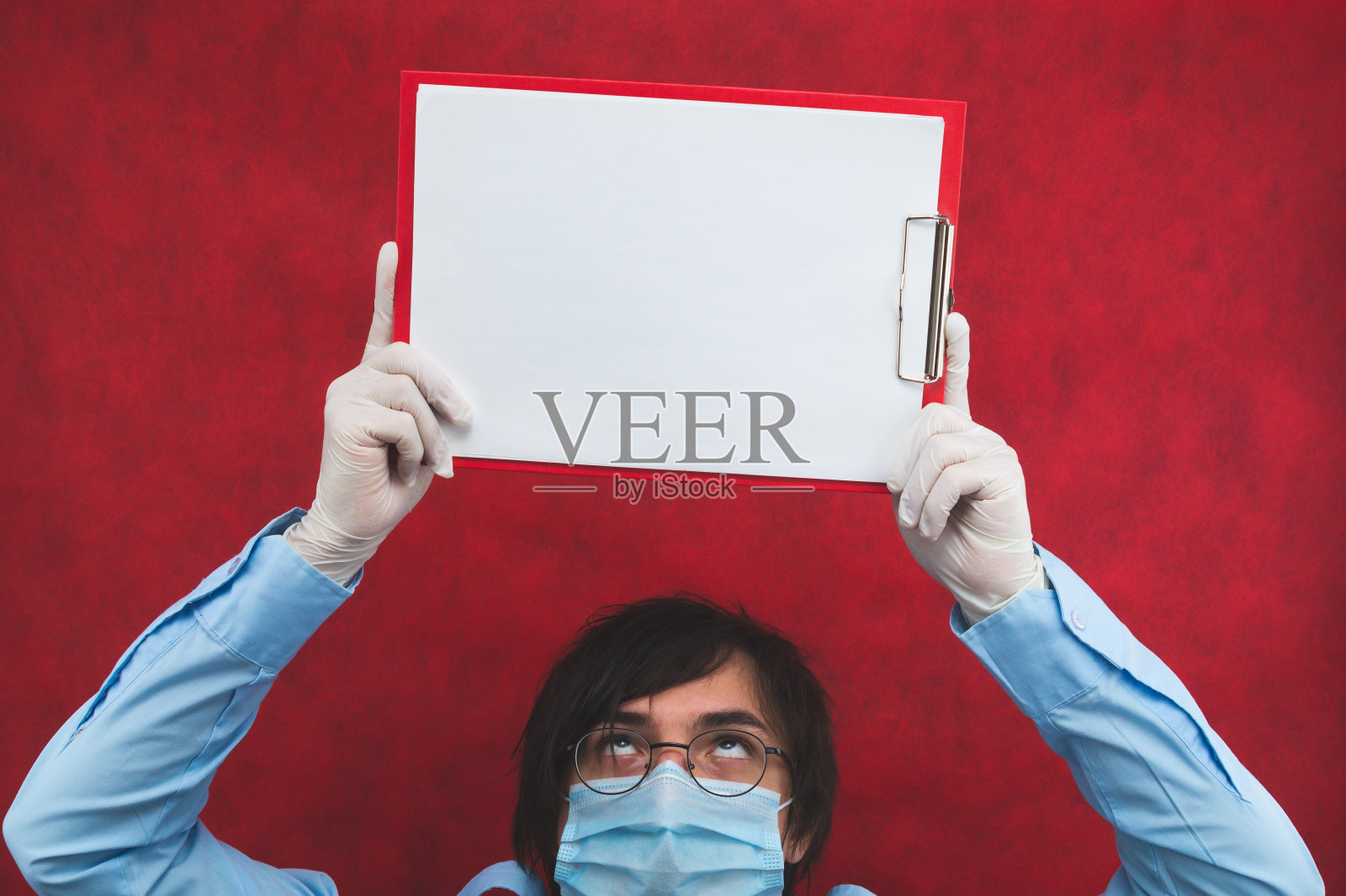 戴着医用口罩的男子拿着白色床单。空的模板。红色背景上的男性肖像。副本的空间。病毒保护措施照片摄影图片