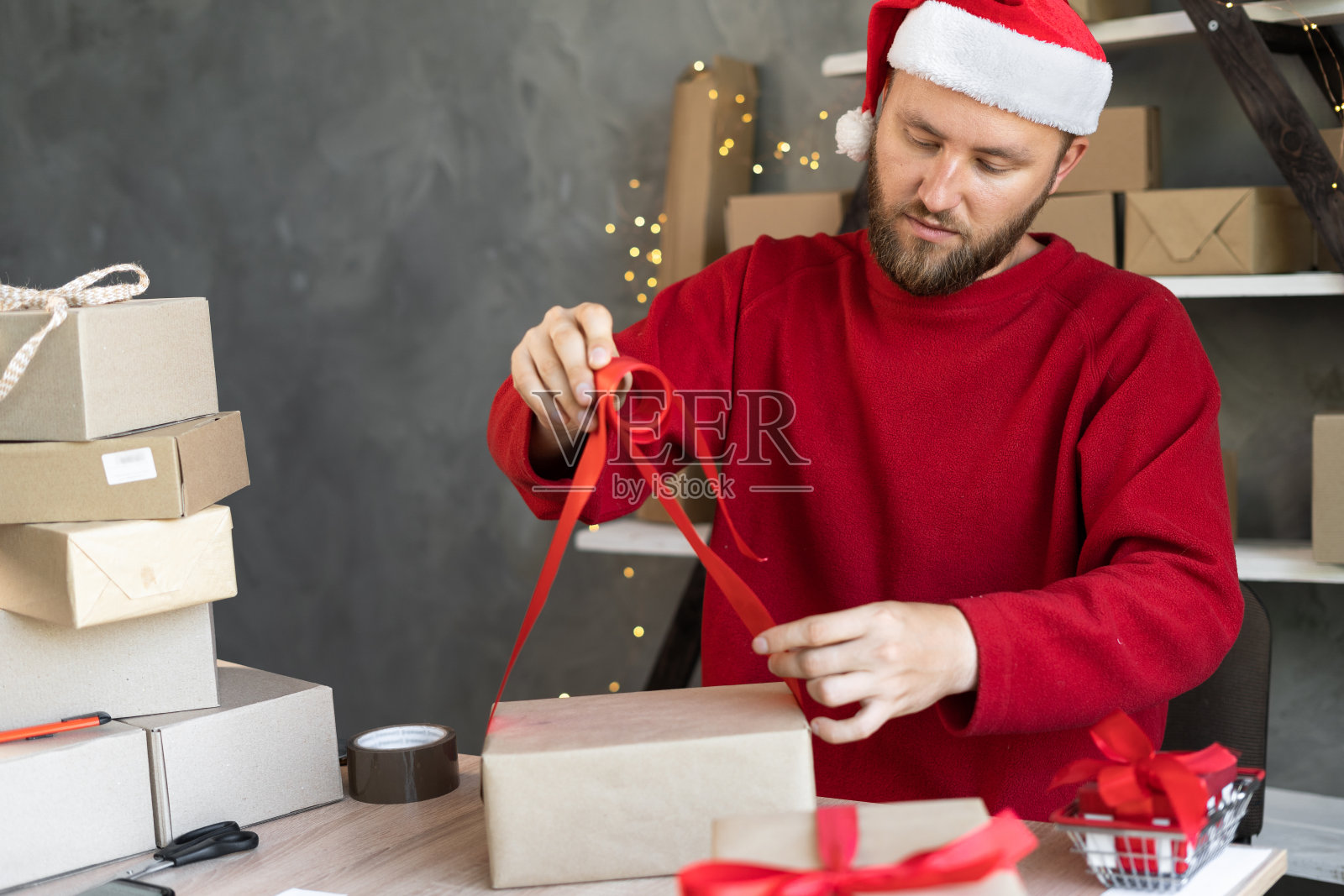 一名戴着圣诞帽的男子在仓库里为准备发货的箱子准备订单。出售照片摄影图片