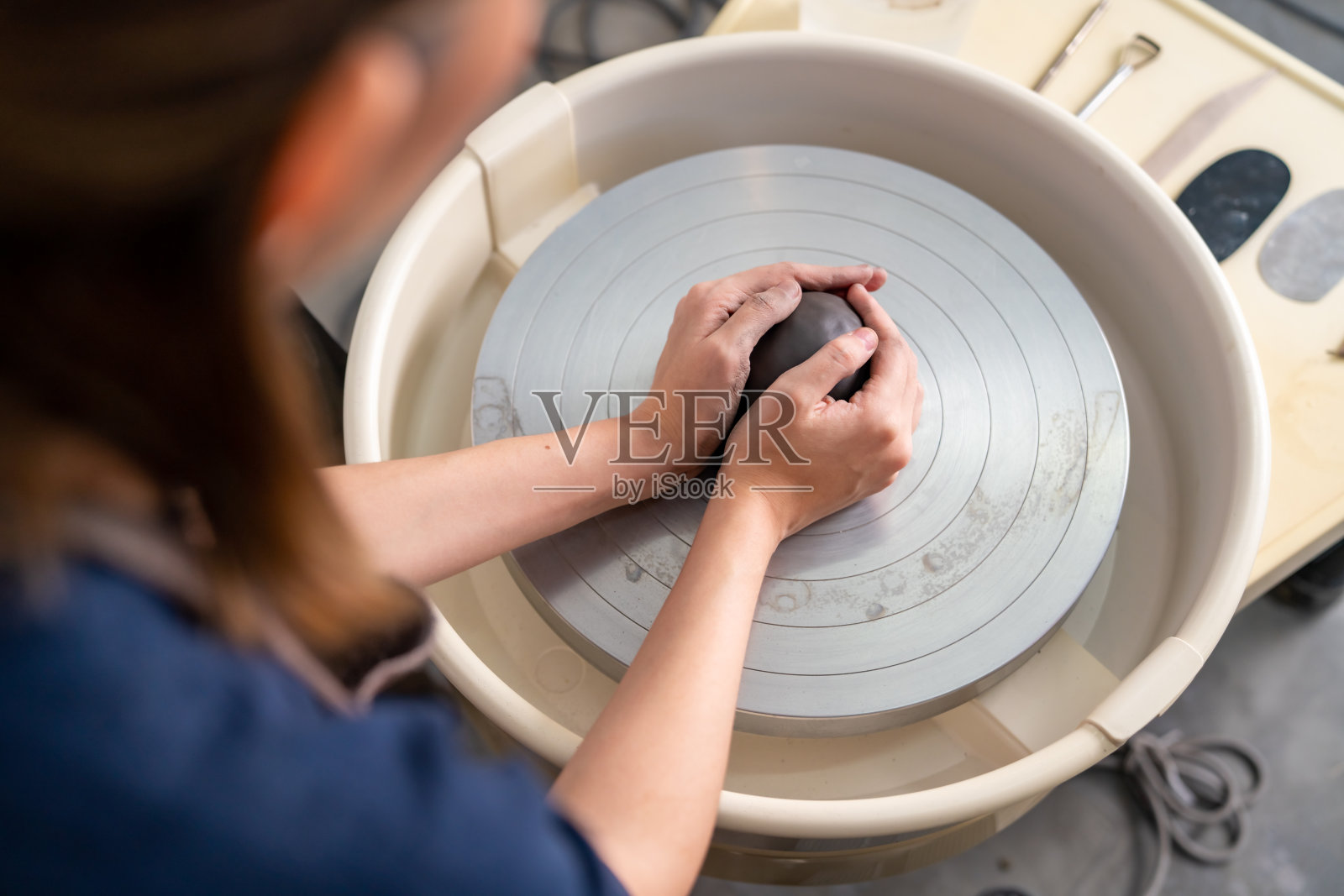 近距离的亚洲妇女雕刻家艺术家手雕刻的陶艺车轮上的粘土在陶瓷工作室。照片摄影图片