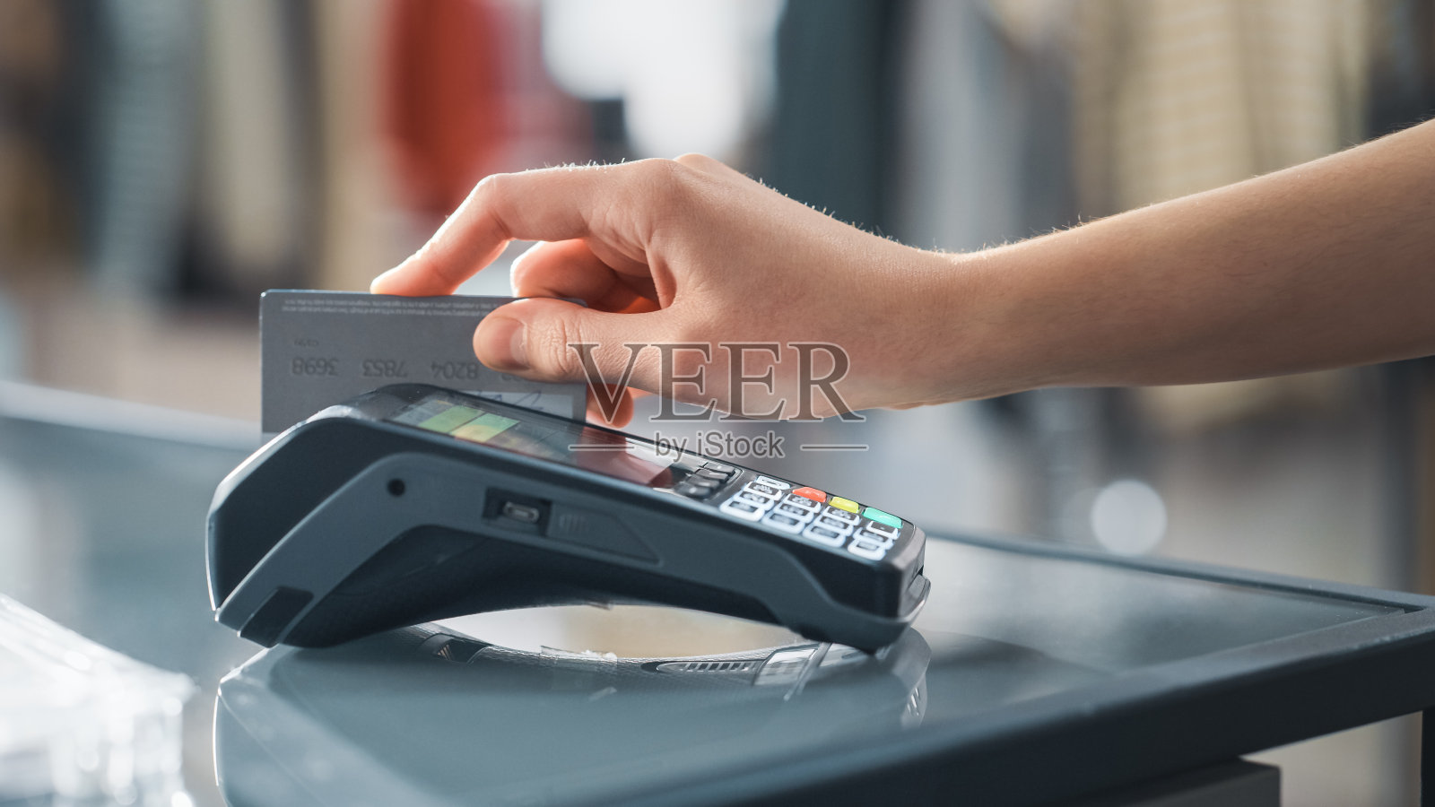 服装店:顾客在柜台购买衣服，通过无线NFC银行终端支付信用卡。时尚时尚商店与时尚设计师品牌。近距离聚焦手部。照片摄影图片