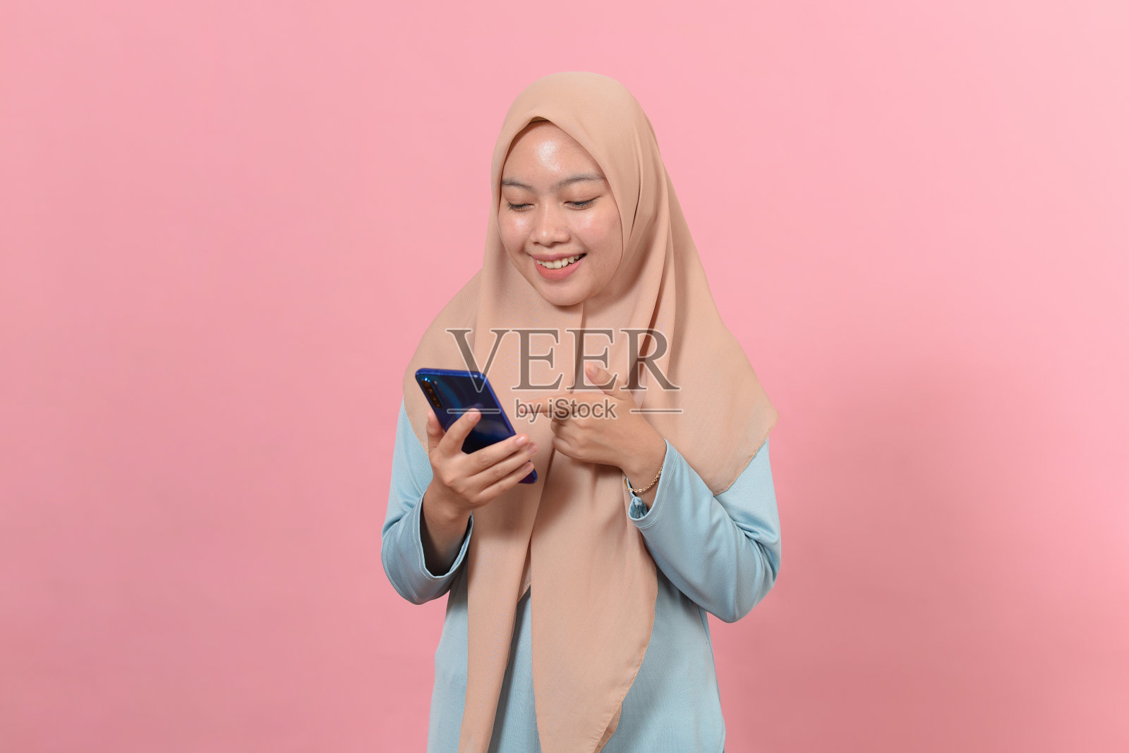 快乐微笑的年轻穆斯林妇女手中拿着智能手机，看着屏幕照片摄影图片