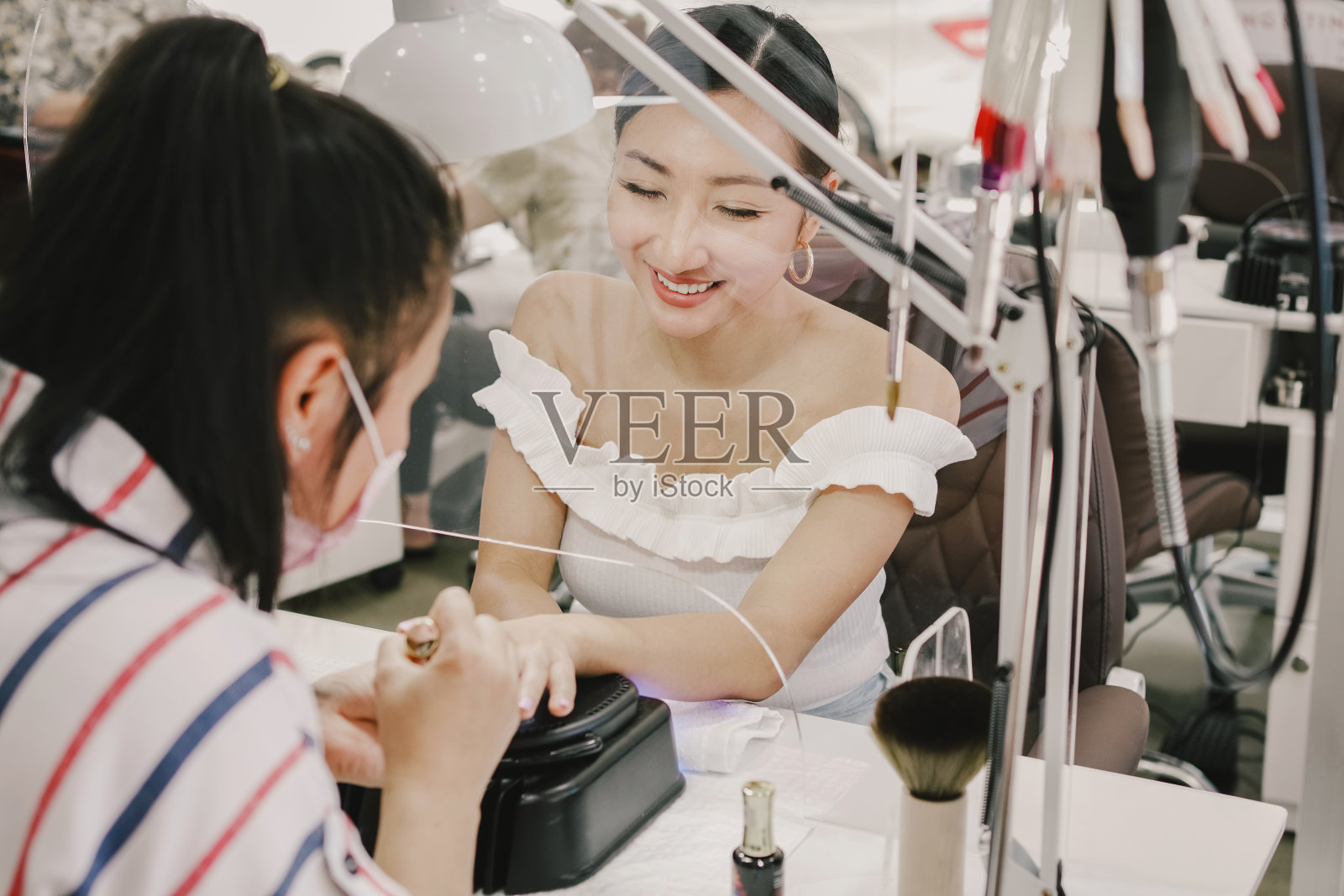 亚洲女性客户在美甲沙龙修指甲，带有防护屏，社交距离covid-19大流行程序，重新开办小企业，健康和美容生活理念照片摄影图片