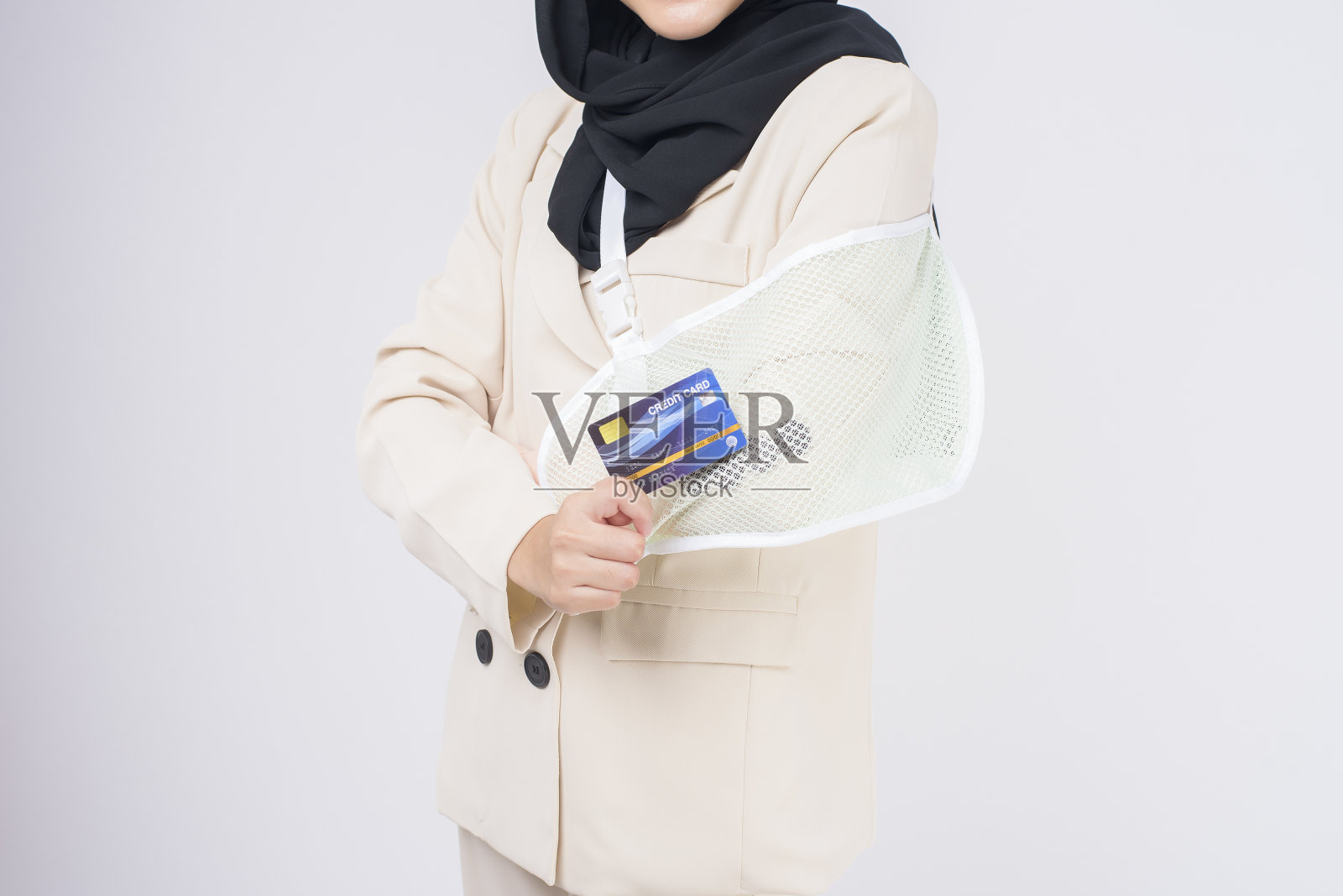 一个年轻的穆斯林妇女的肖像与受伤的手臂在一个吊带在工作室的蓝色背景。照片摄影图片