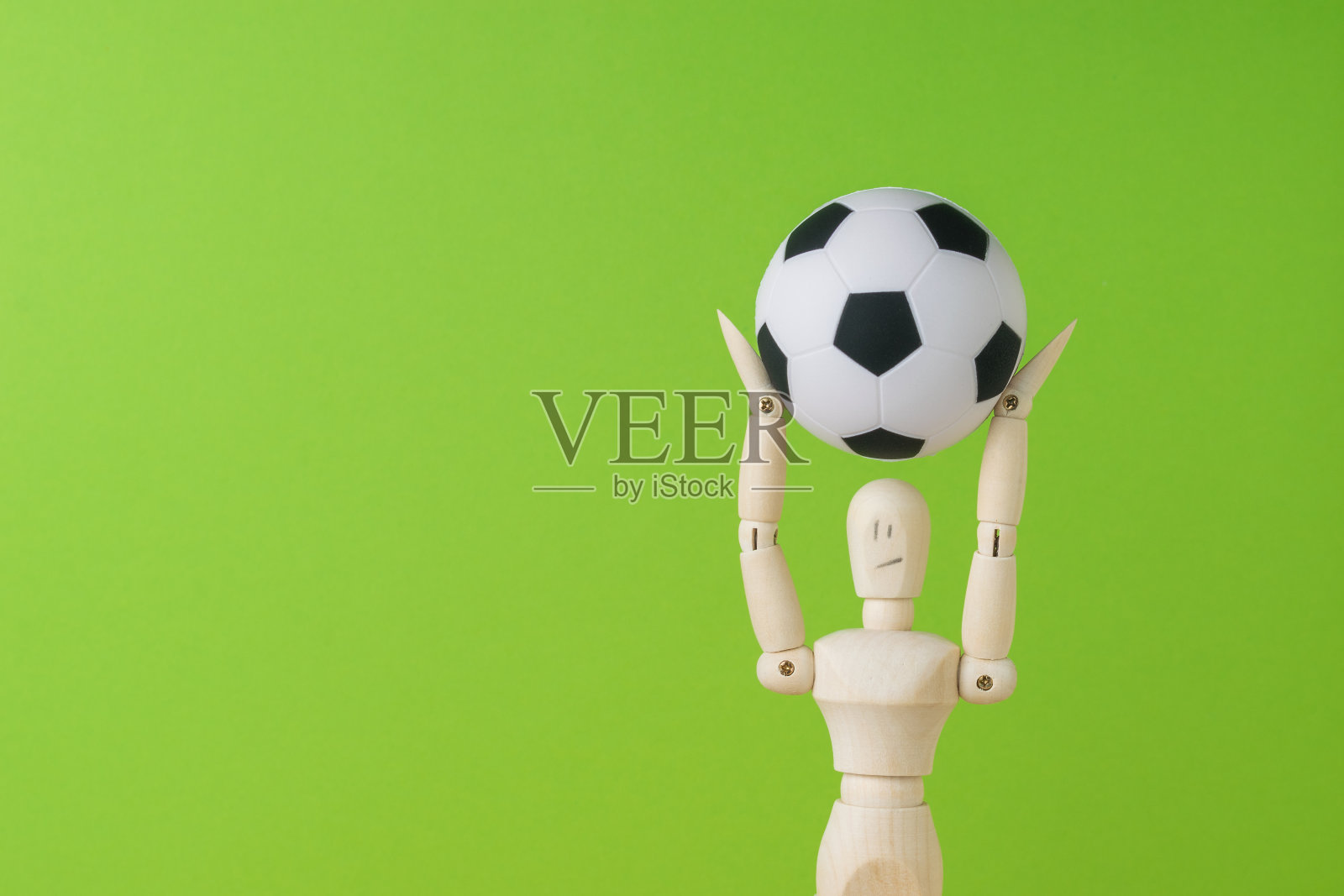 绿色背景上一个木头人手里的足球。空间的文本。照片摄影图片