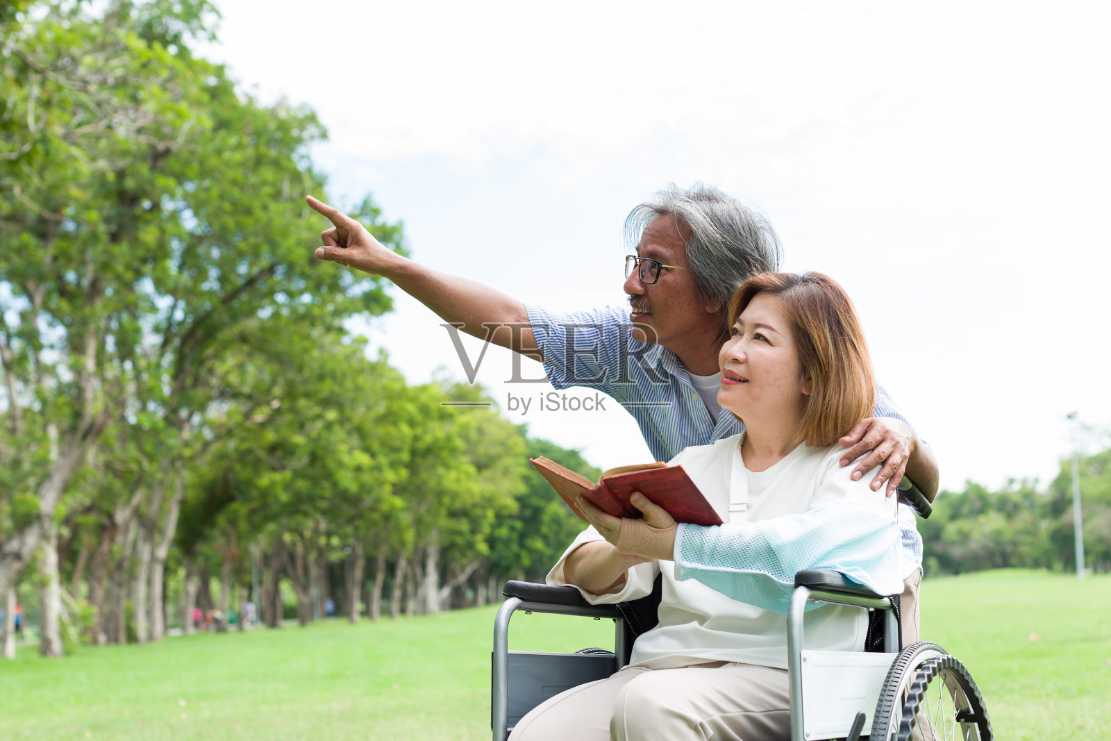 一位亚洲老人坐在轮椅上照顾年迈生病的妻子，他受伤的手臂裹在石膏里。亚洲老年夫妇花时间和放松一起户外照片摄影图片