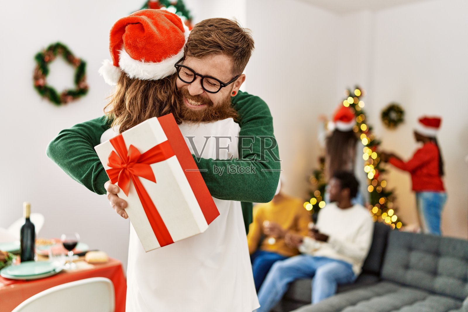 一群年轻人在圣诞节聚会。情侣们拿着礼物，在家里拥抱。照片摄影图片