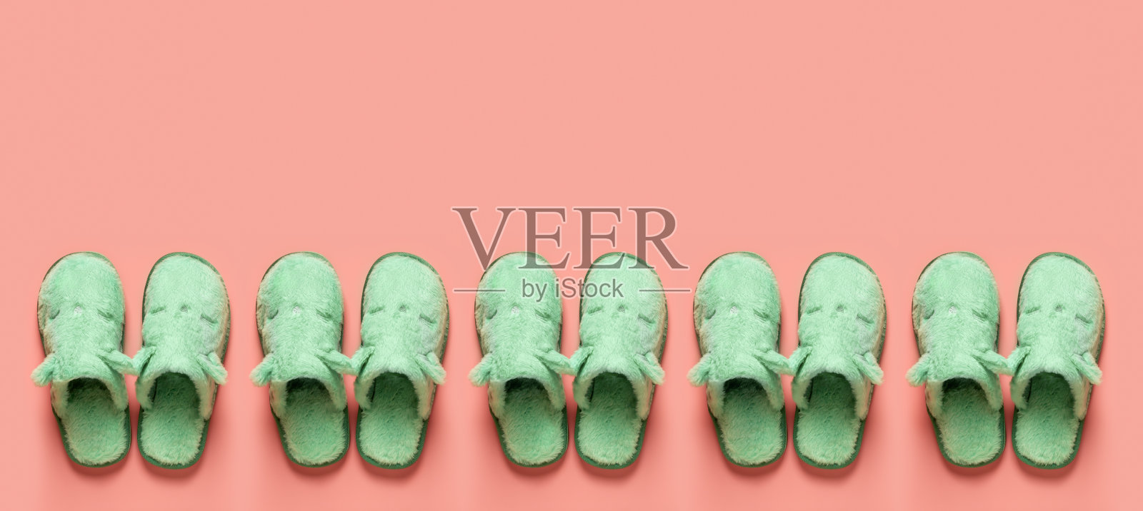 猫脸拖鞋在一排在橘色背景与复制空间。珊瑚色表面的青瓷绿色舒适家居拖鞋图案。有趣舒适的室内鞋概念。平的。照片摄影图片