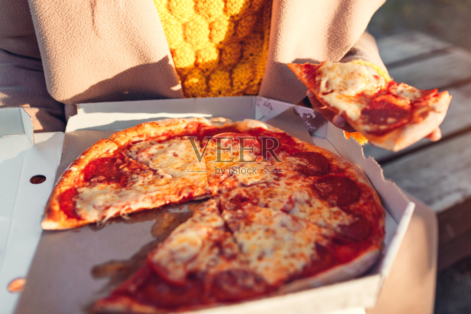 盒装意大利辣香肠披萨。女人在户外拿着美味的切片。热的点心照片摄影图片