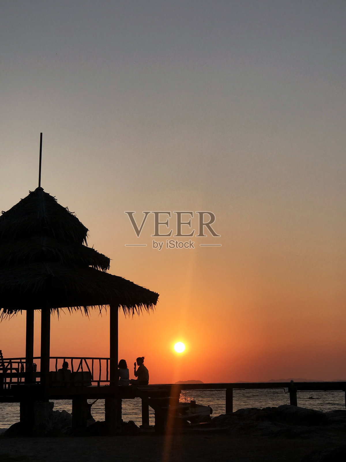 海滩上的日落，人们坐在平房里。照片摄影图片