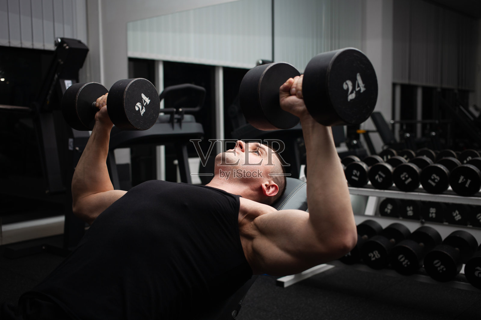 男人在体育馆的模拟器上用哑铃做练习。运动员，健美运动员，健身教练。强壮性感的身体。谎言照片摄影图片