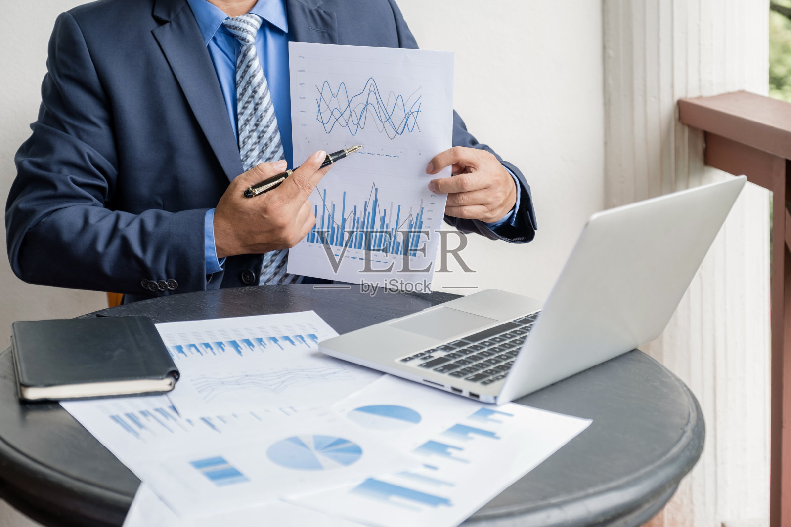 商人手中拿着笔，在家里用笔记本电脑分析图表，制定具有挑战性的业务目标和计划实现新的目标照片摄影图片