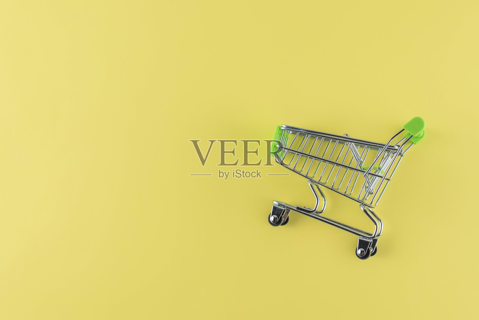 黄色背景上的绿色购物车。复制空间，文本的自由空间。照片摄影图片