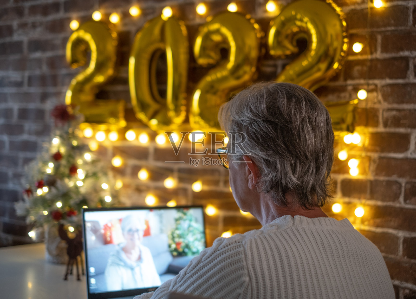 女人用笔记本电脑视频通话。圣诞快乐，新年快乐，桌子上的小圣诞树和2022金色充气数字照片摄影图片