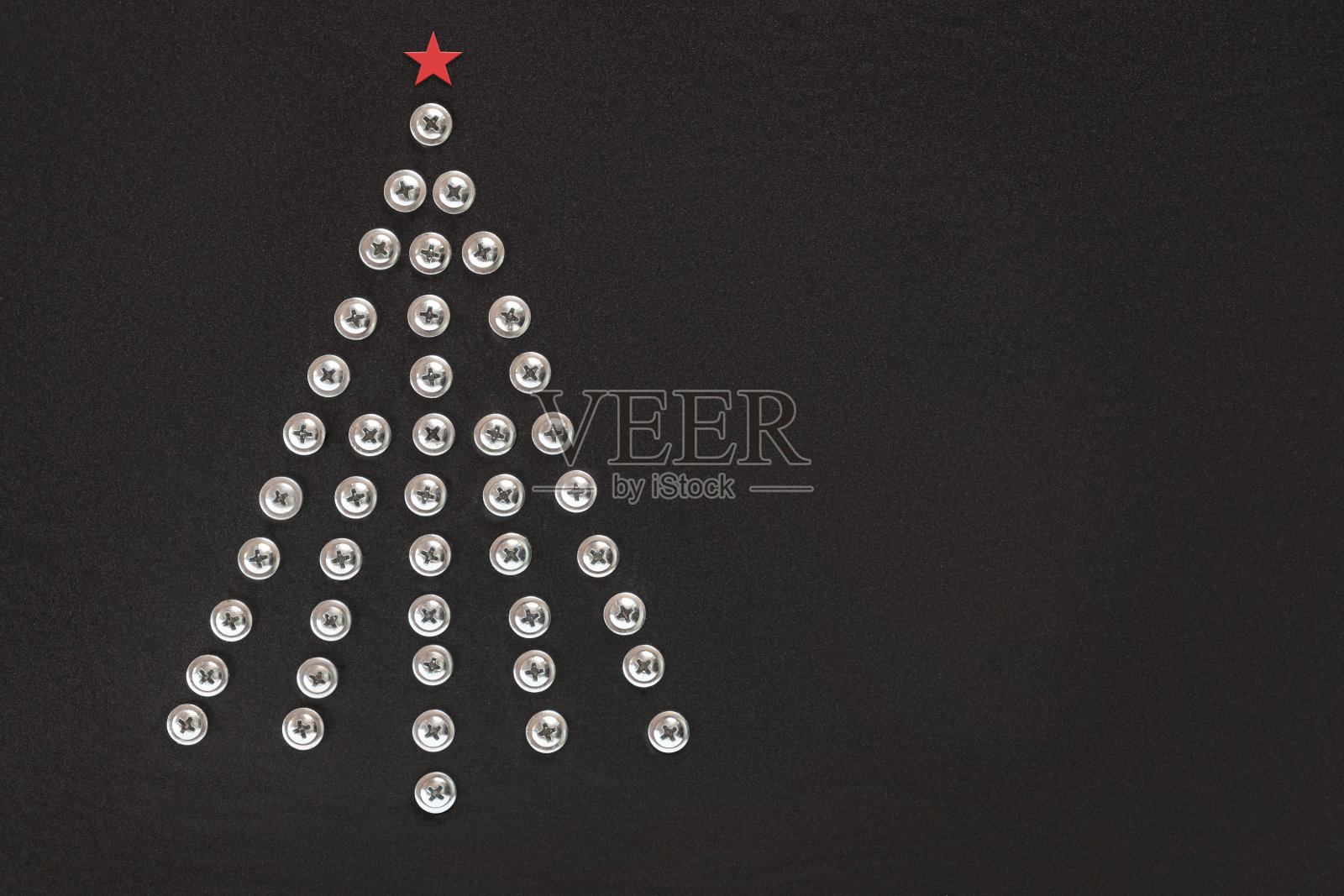 黑色背景上的一棵钉满螺丝钉的圣诞树。平的。副本的空间。由建筑工具制成的不寻常圣诞树。创意工业贺卡。构建、修复的概念。车间。前视图。照片摄影图片