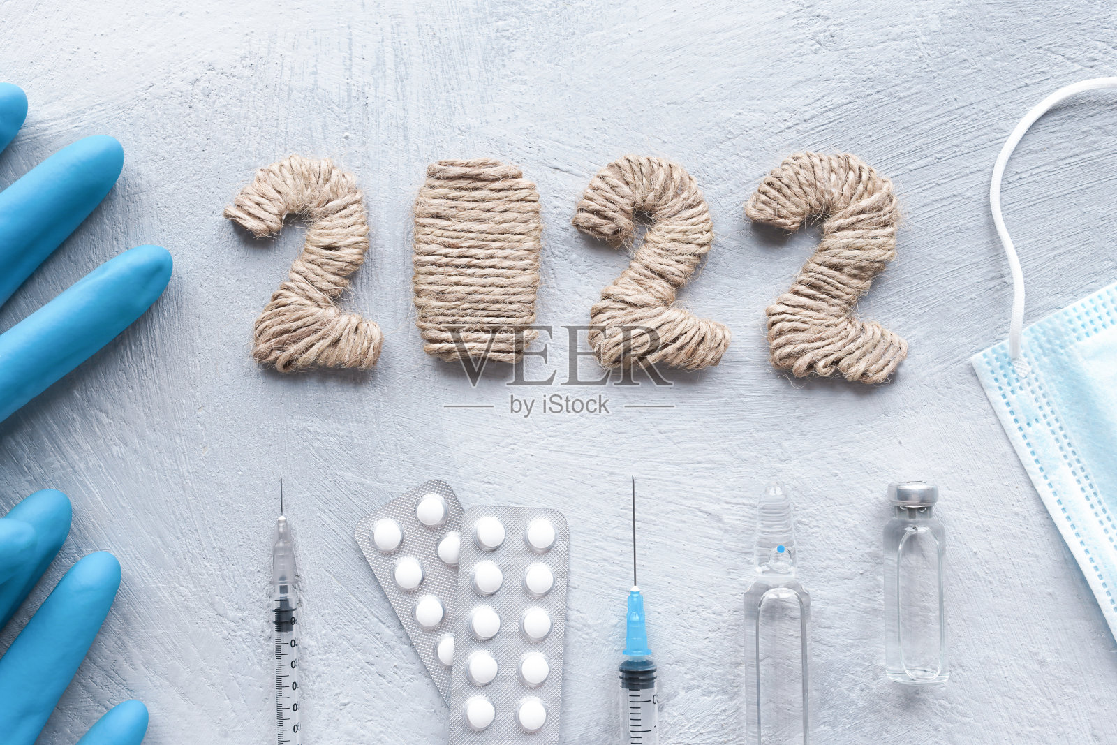 以节日为背景，在灰色混凝土桌子上摆放着治疗设备、药丸、注射器、手套、口罩和注射设备，上面写着数字2022。圣诞节医疗卡片。照片摄影图片