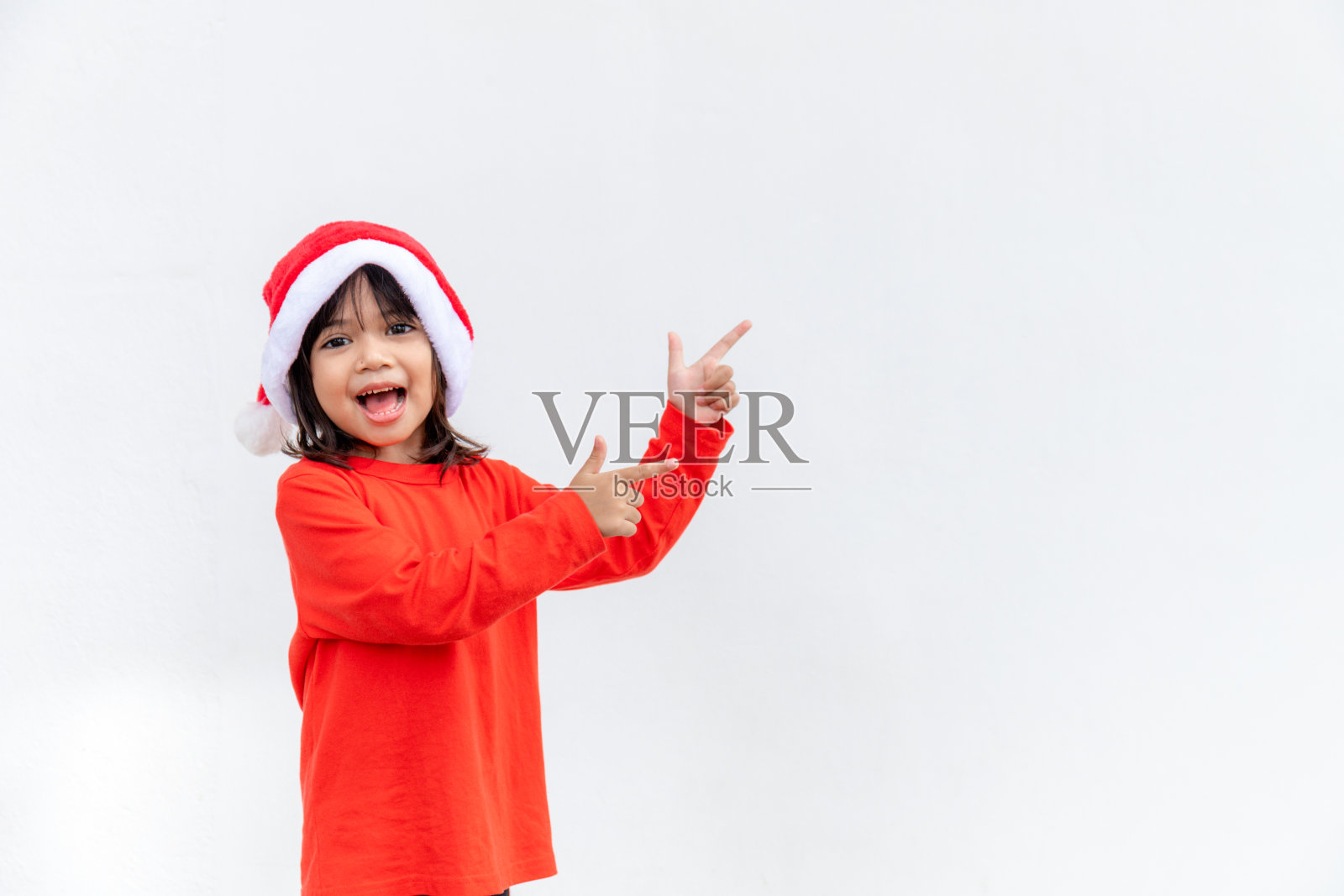 亚洲小女孩在白色背景上红色的圣诞老人帽子。照片摄影图片