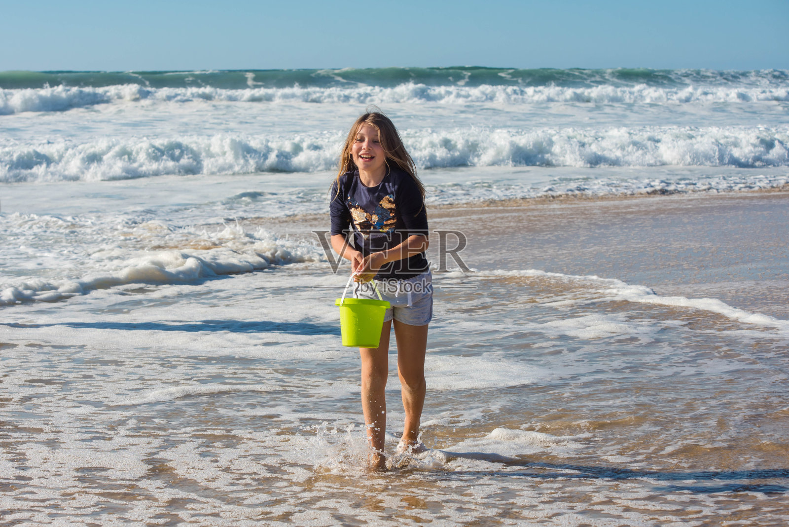 小女孩在海边玩她的水桶照片摄影图片